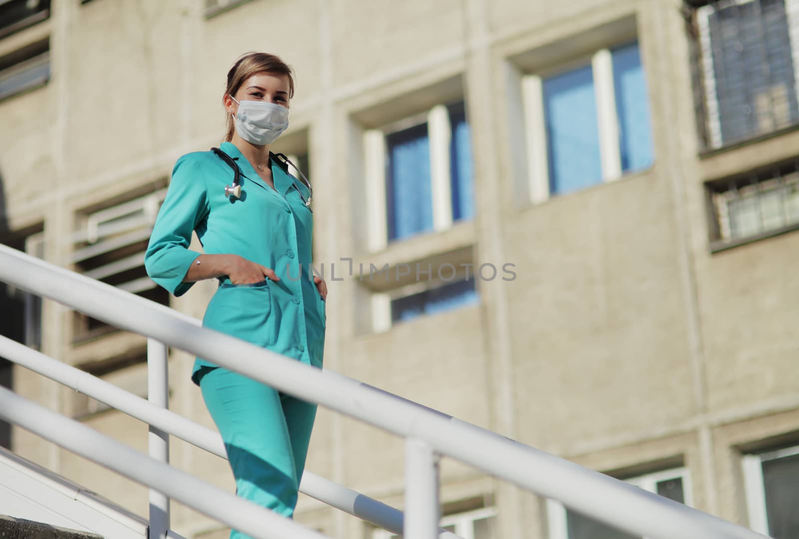Female doctor or nurse in a protective face mask walking up the stairs by selinsmo