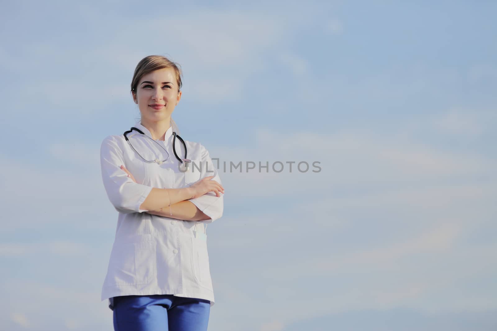 Portrait of a beautiful female doctor or nurse against blue sky with clouds by selinsmo