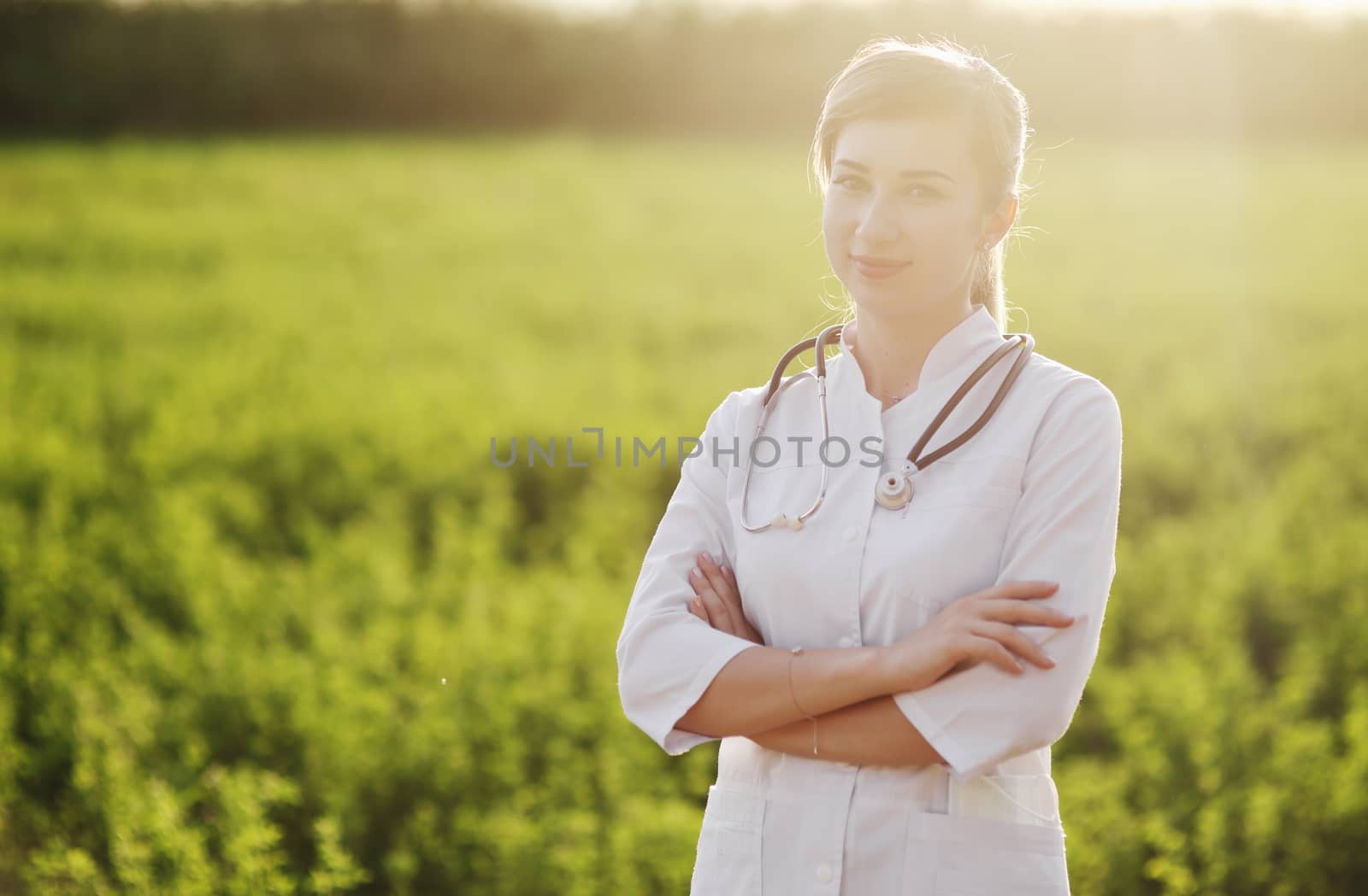 Portrait of a beautiful female doctor or nurse on green grass background. Prevention Covid-19 healthcare concept. Stethoscope over the neck. Woman, girl.