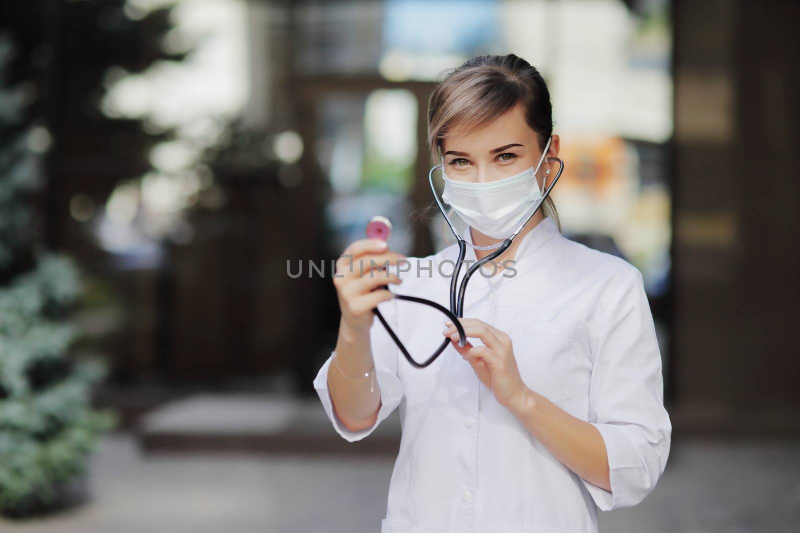 A woman doctor in a face medical mask with stethoscope ready to check lungs by selinsmo