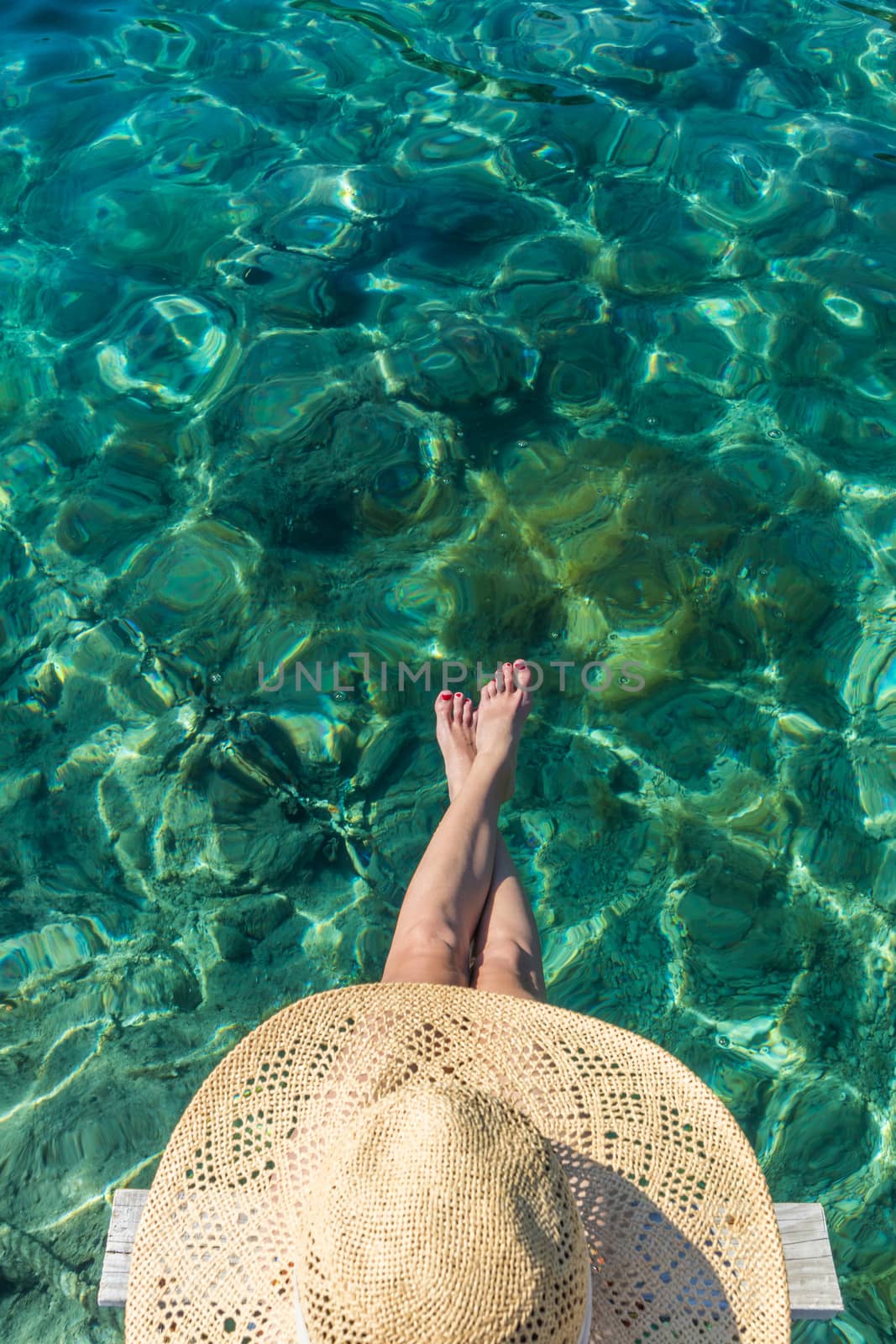 Graphic image of top down view of woman wearing big summer sun hat relaxing on small wooden pier by clear turquoise sea by kasto