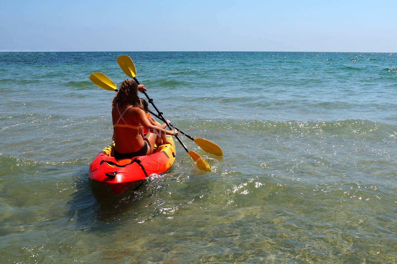 woman with two children kayaking in the sea, back view