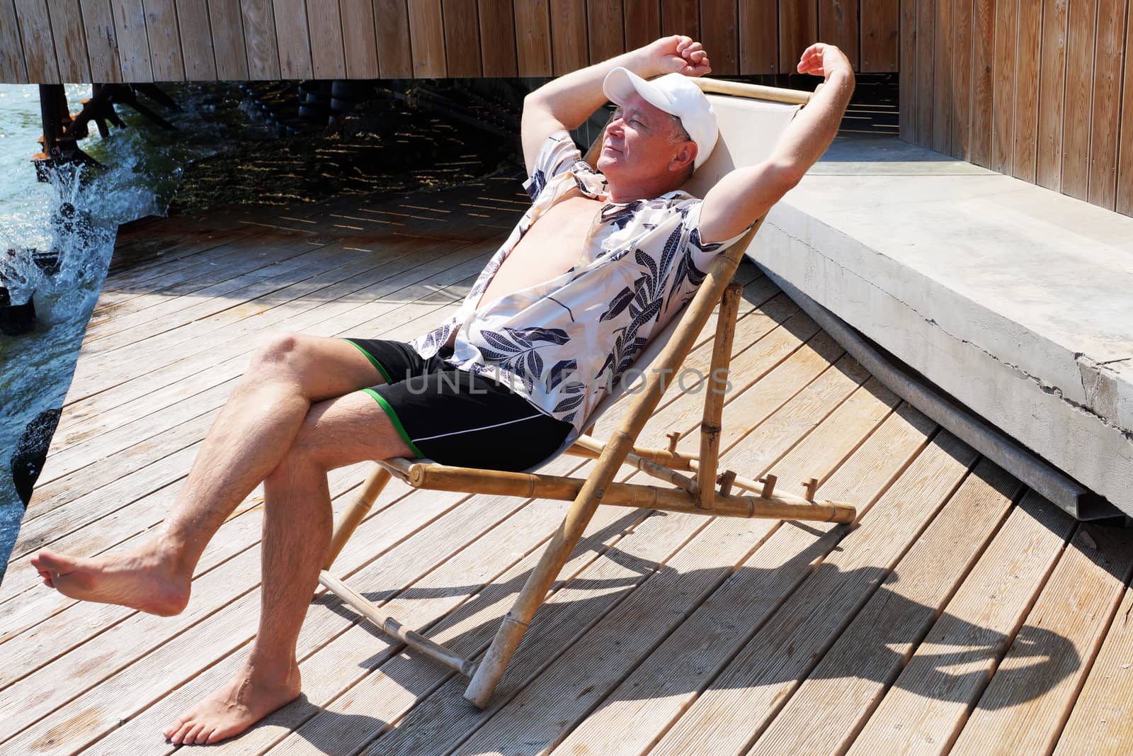 smiling man resting on a sun lounger on the patio by Annado