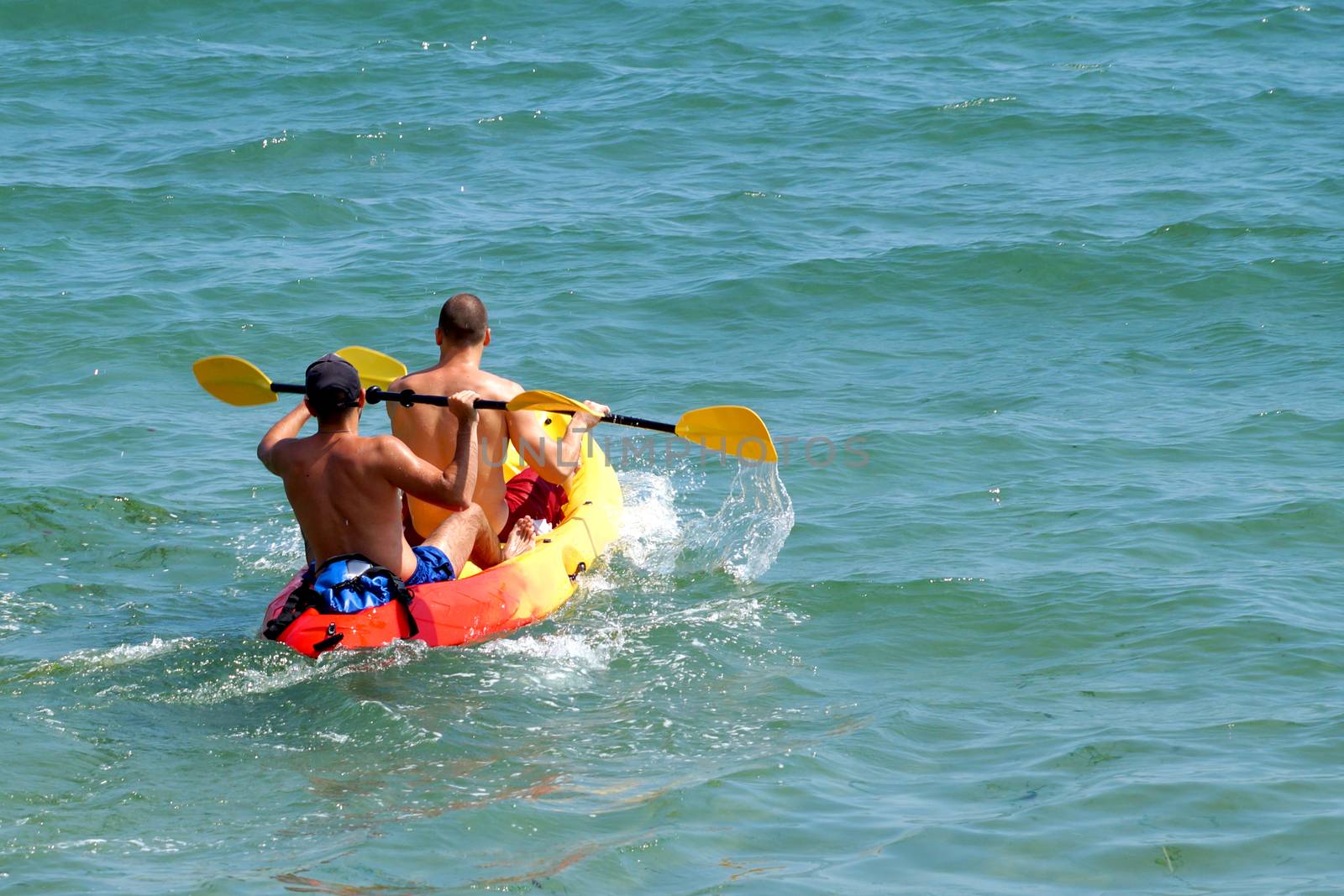 two young men are sailing on a kayak in the sea, rear view