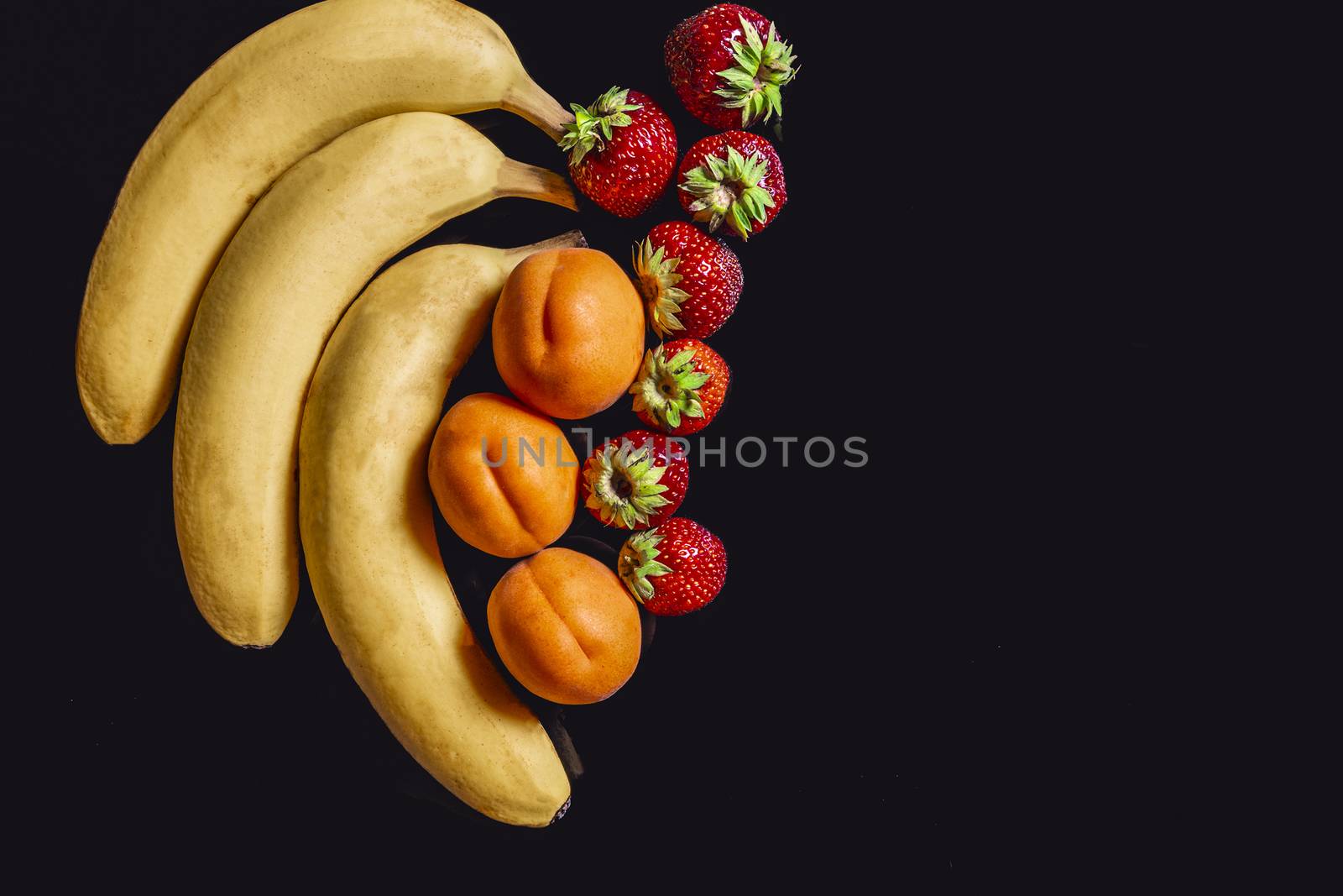 Bananas, apricots and strawberries against a black background with reflection