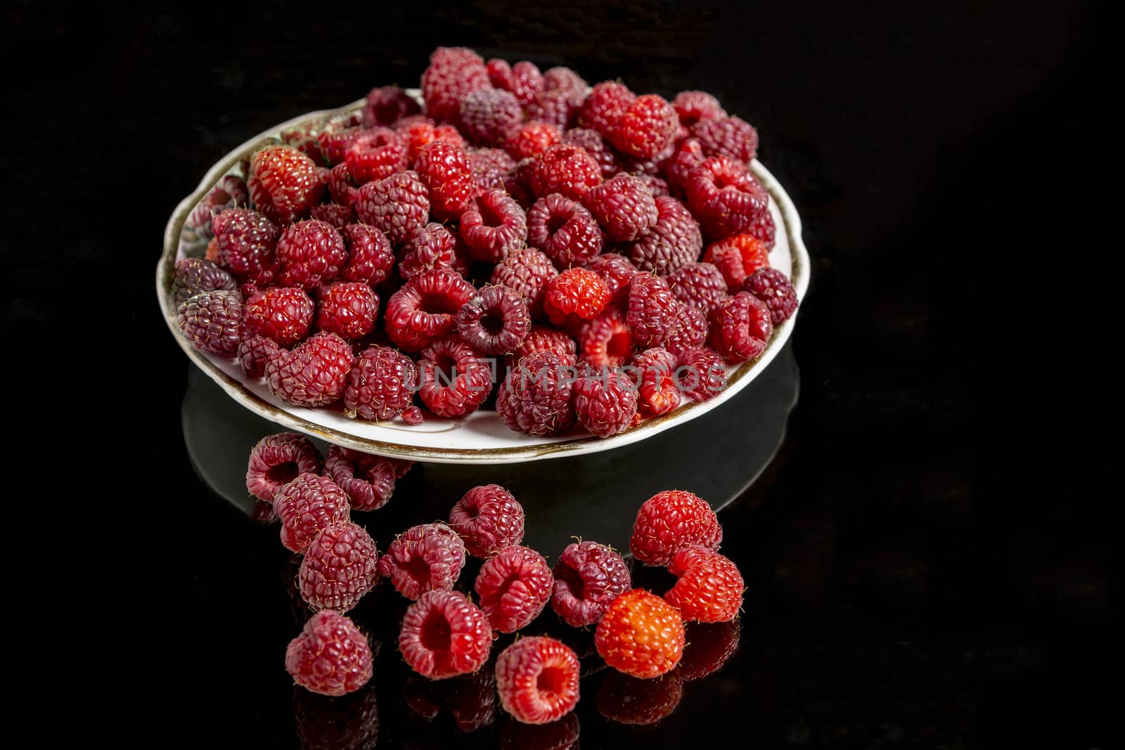 Raspberry berry on a white plate against a black background with reflection