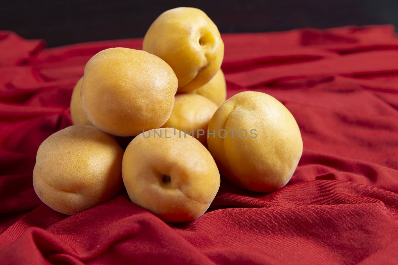 A pile of apricot piles stacked together lie on a red tablecloth against a red background