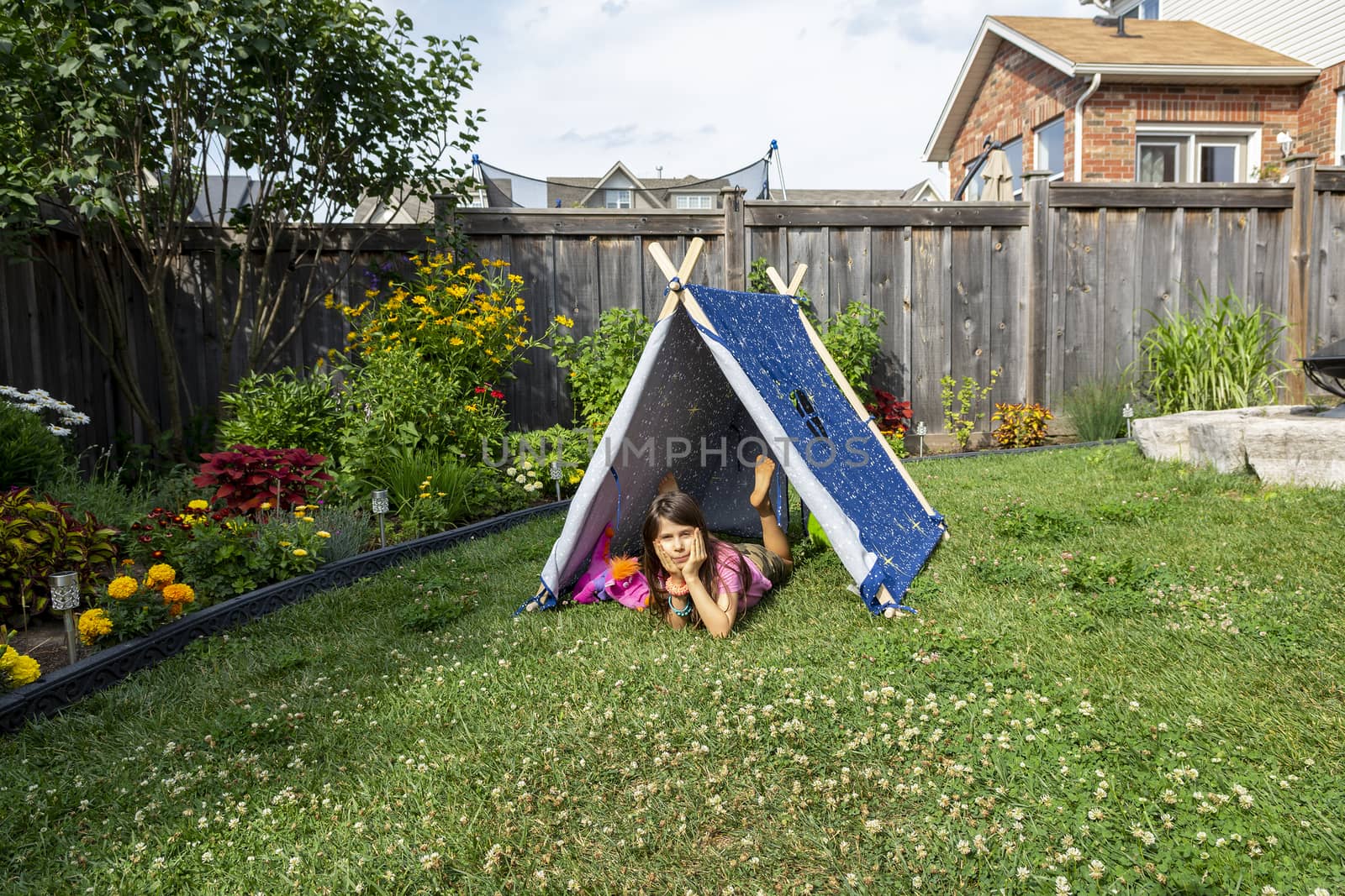 Little girl playing with toys in a tent on the grass in the garden