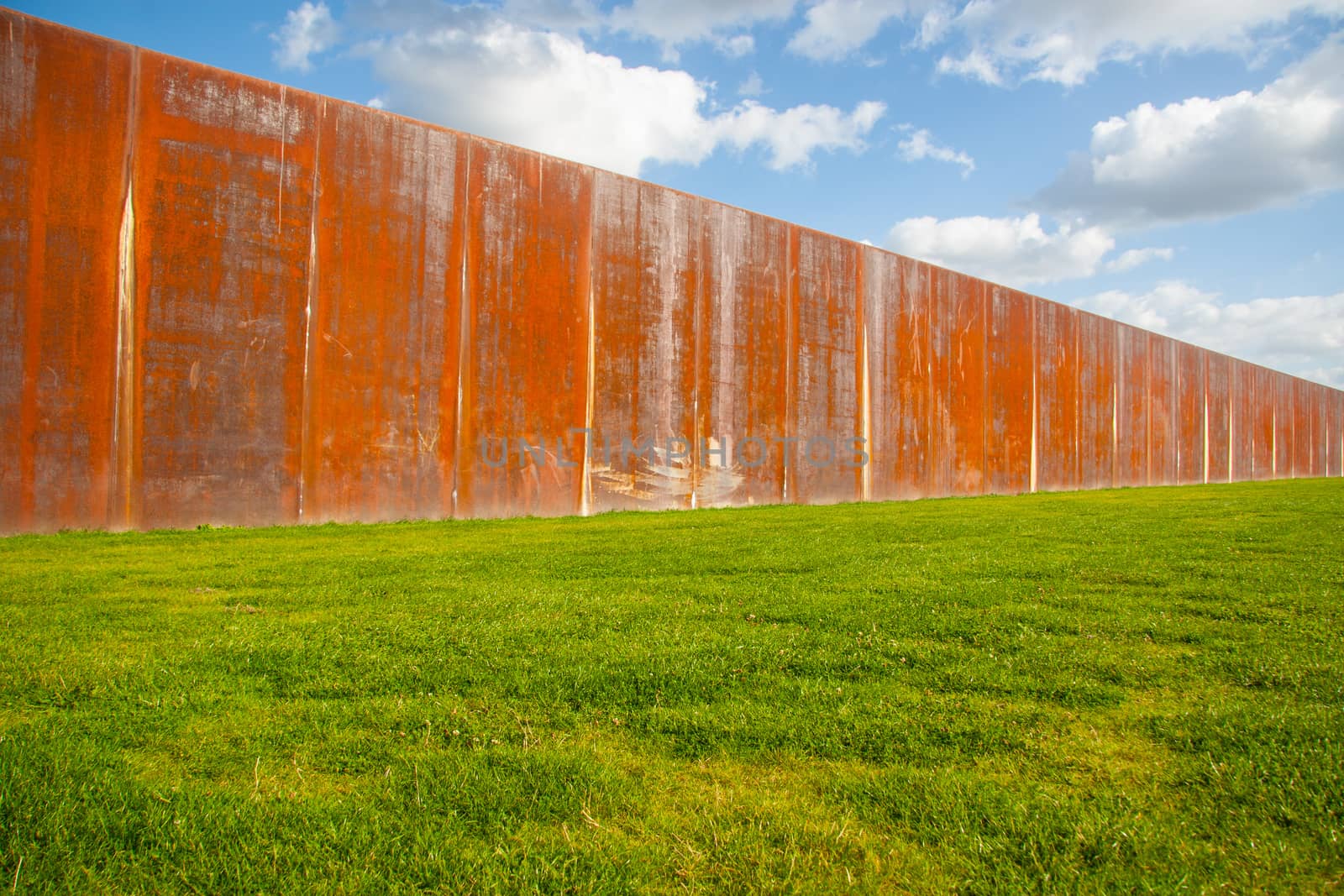 Old rusty metal fence wall on green meadow with blue sky in background