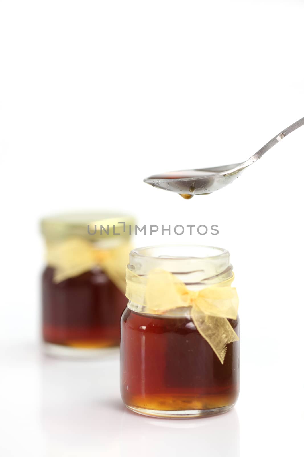 honey dripping from spoon on top of jar, isolated on white background 