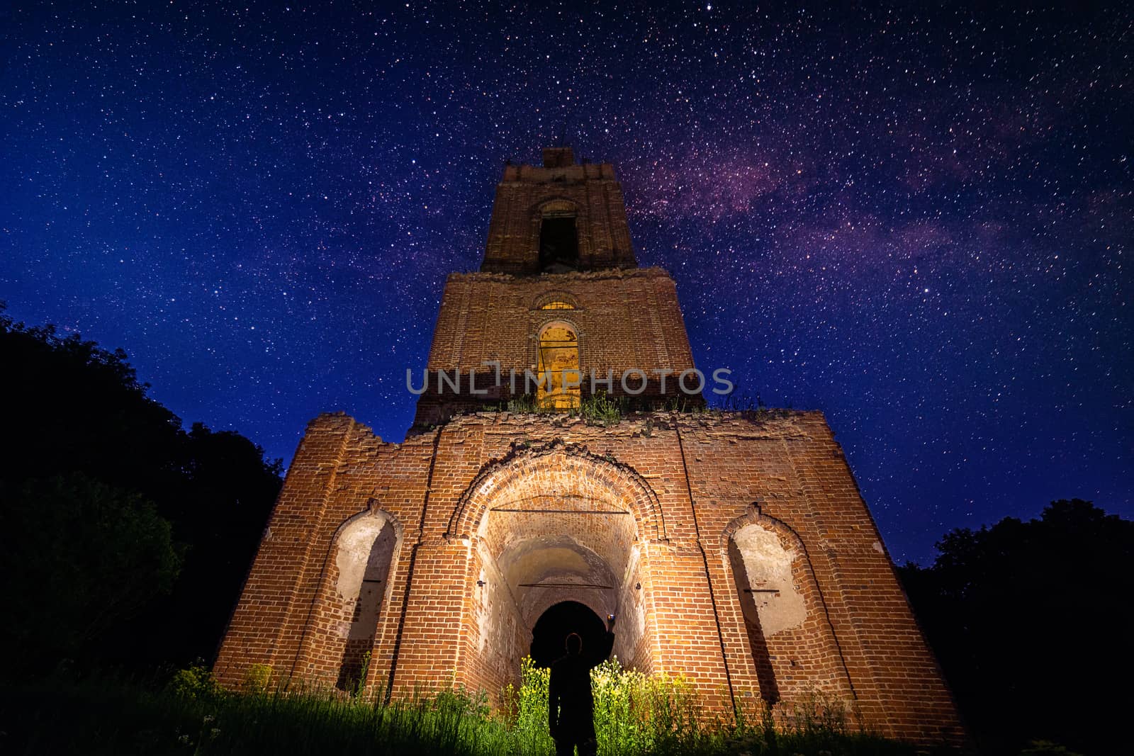 night bell tower ruin in forest at starry night and man with flashlight under it by z1b