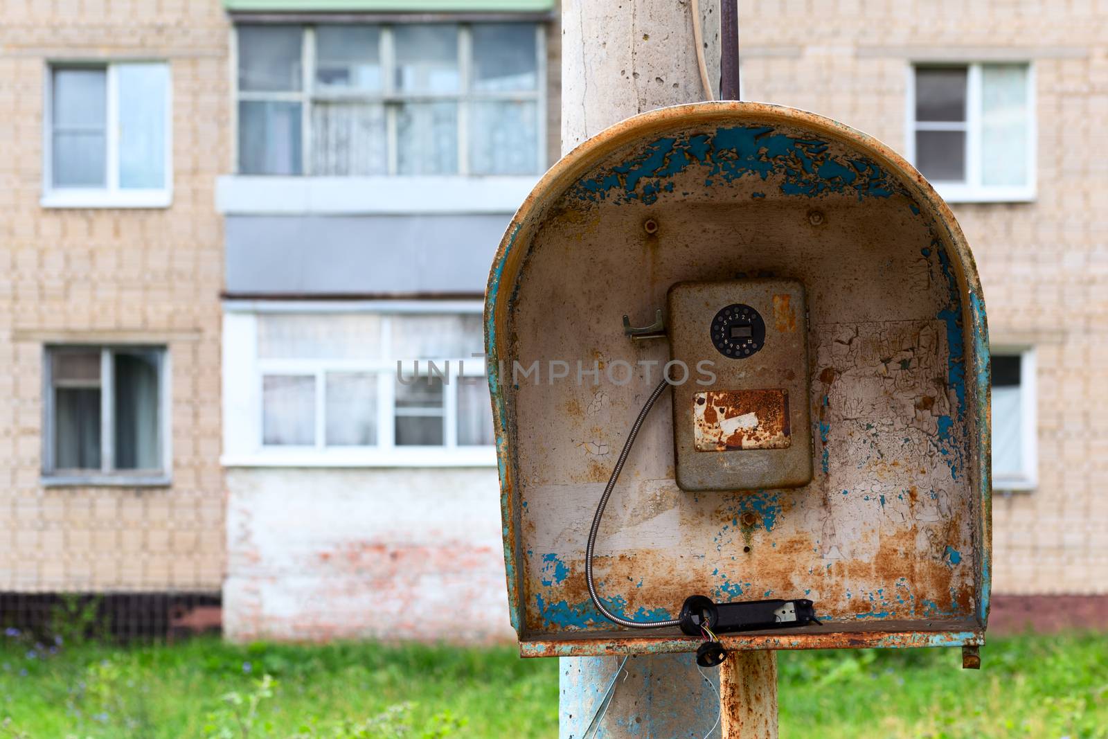 Old public russian wired urban telephone post - useless abandoned and broken. Horizontal shot with selective focus and blurred suburbs condominium house in background.