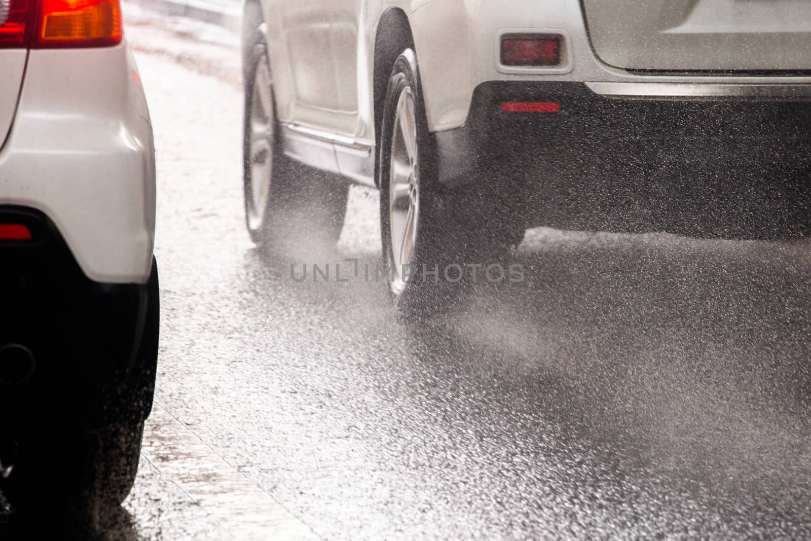 rain water splash flow from wheels of white car moving fast in daylight city with selective focus.