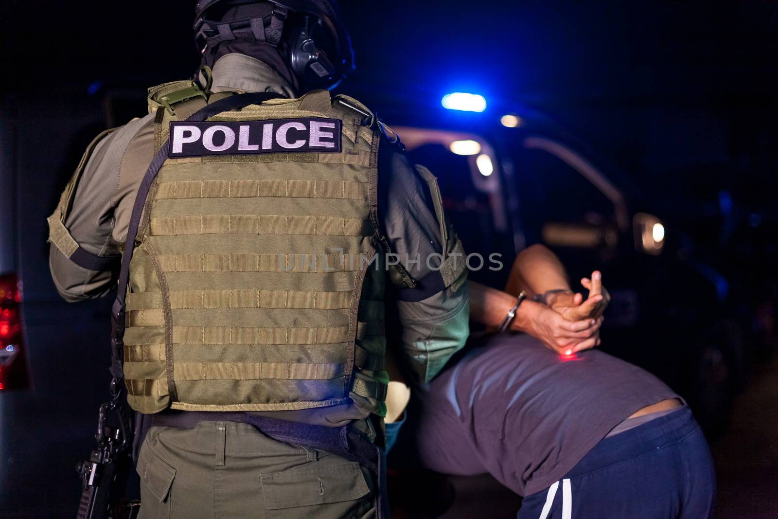 A police officer puts handcuffs on a criminal's hands during an arrest. Police car with flashing lighthouses. copy space