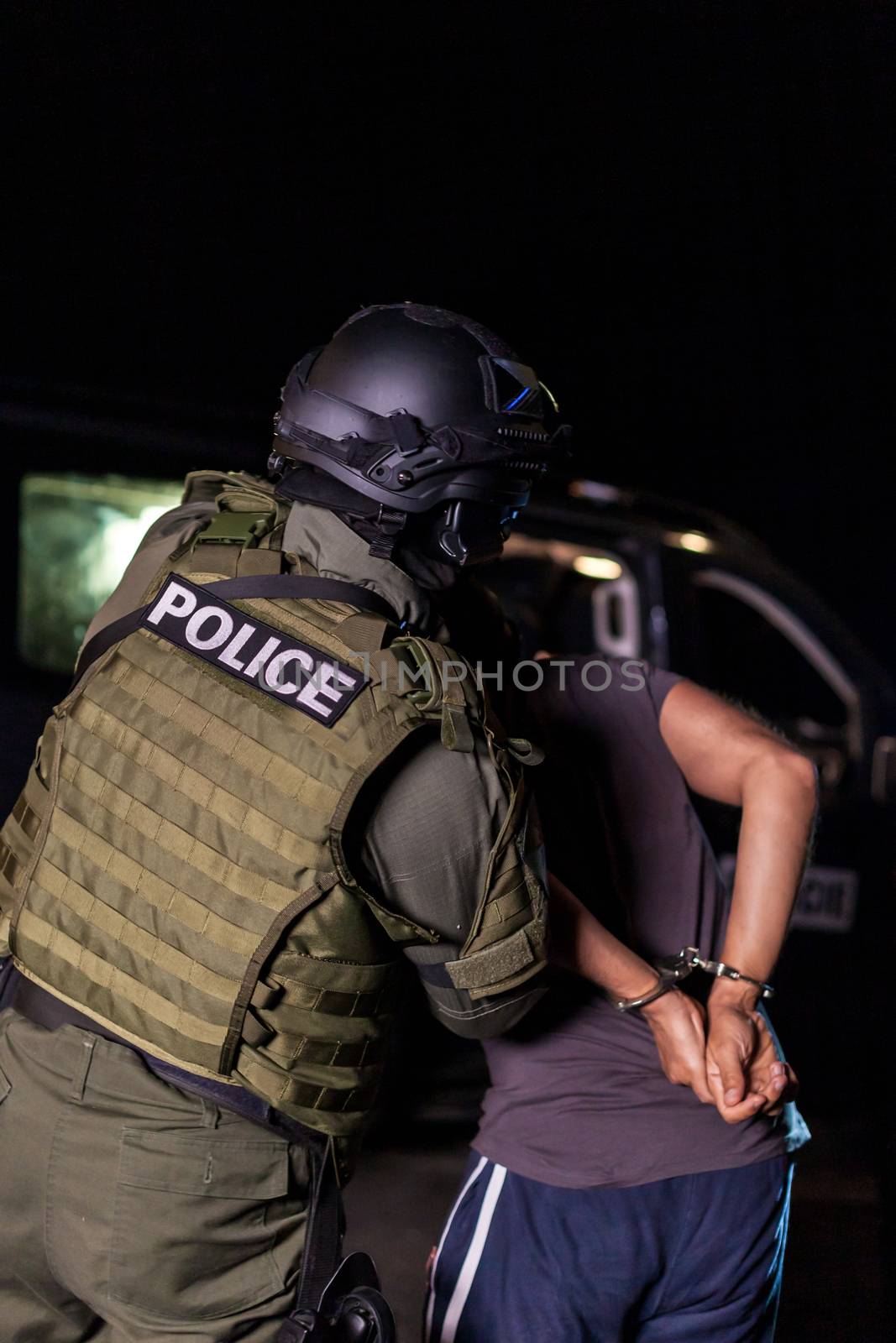 A police officer puts handcuffs on a criminal's hands during an arrest. Police car with flashing lighthouses. Blurried by Edophoto
