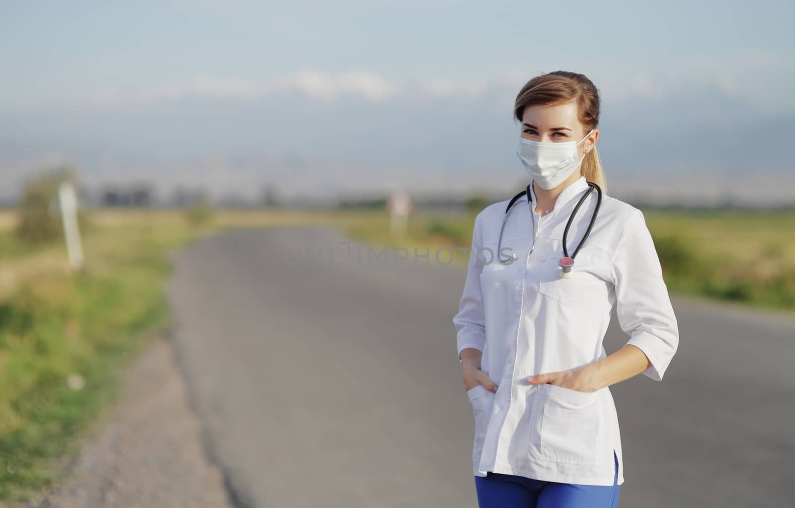 Female doctor or nurse wearing a protective face mask next to a rural road. Safety measures against the coronavirus. Prevention Covid-19 healthcare concept. Stethoscope over the neck. Woman, girl.