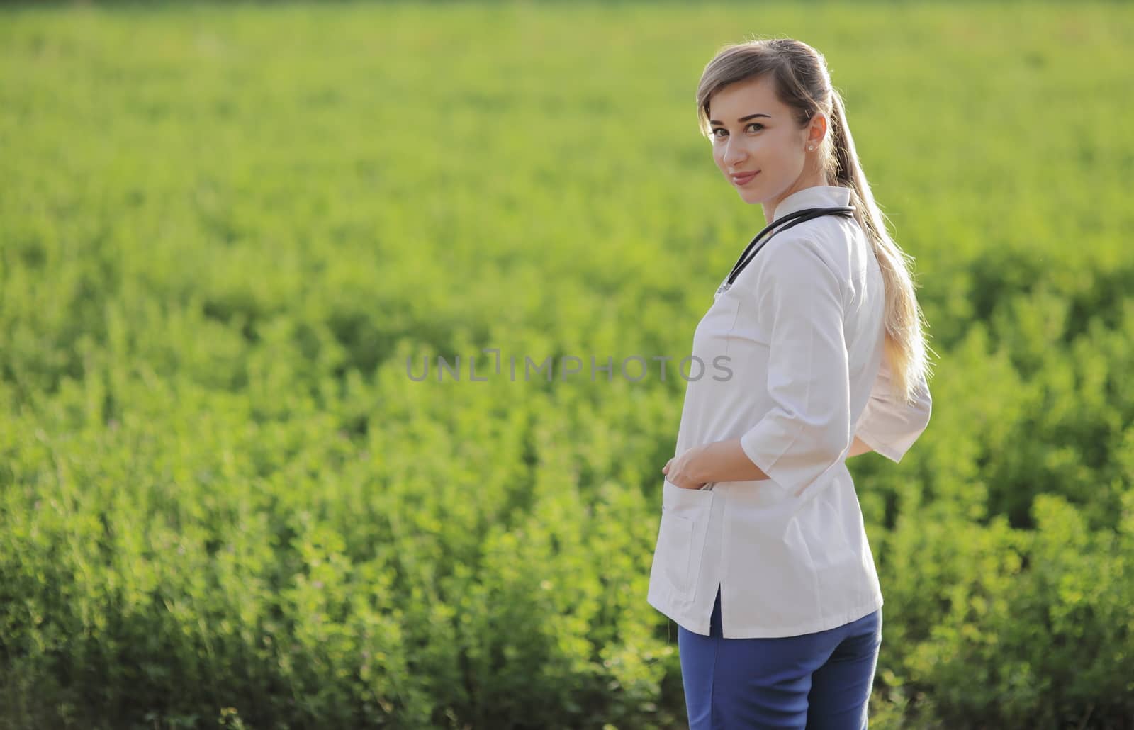 Portrait of a beautiful female doctor or nurse on green grass background by selinsmo