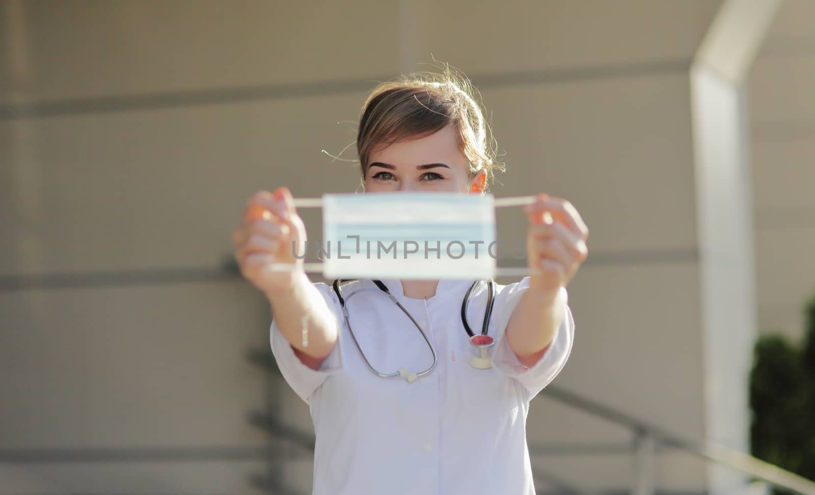 Young woman doctor or nurse showing medical face mask close up. Prevention Covid-19 healthcare concept. Stethoscope over the neck. Female, girl.