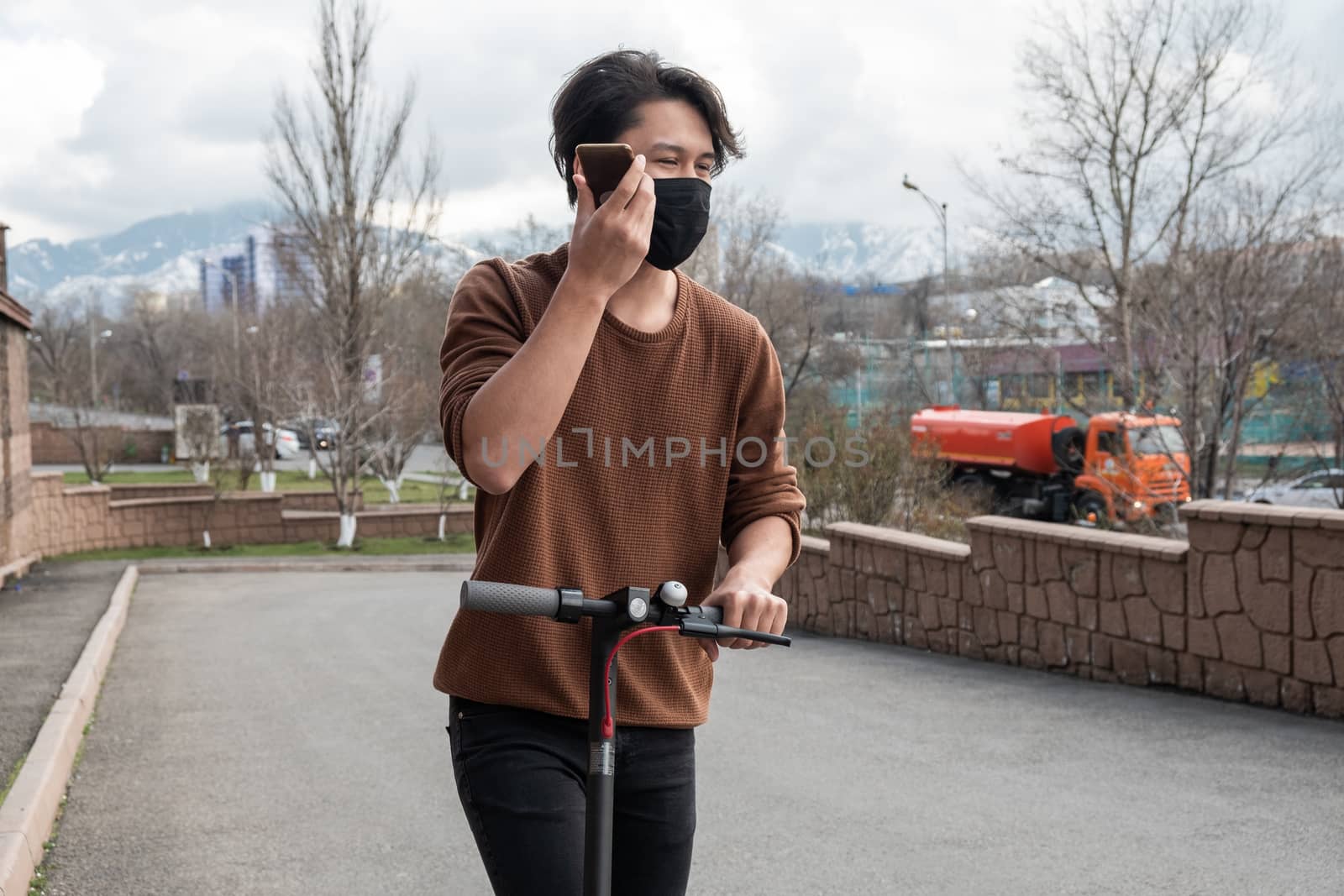 Young man riding a scooter and talking by mobile phone in the city