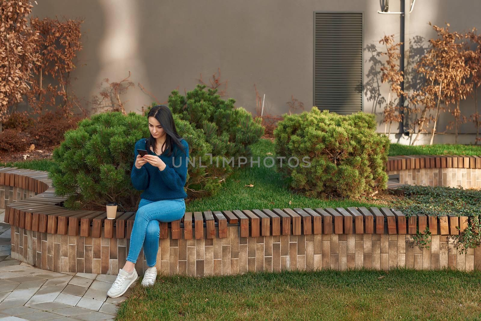 Concentrated female is messaging by her smartphone opposite the beautiful dooryard by monakoartstudio