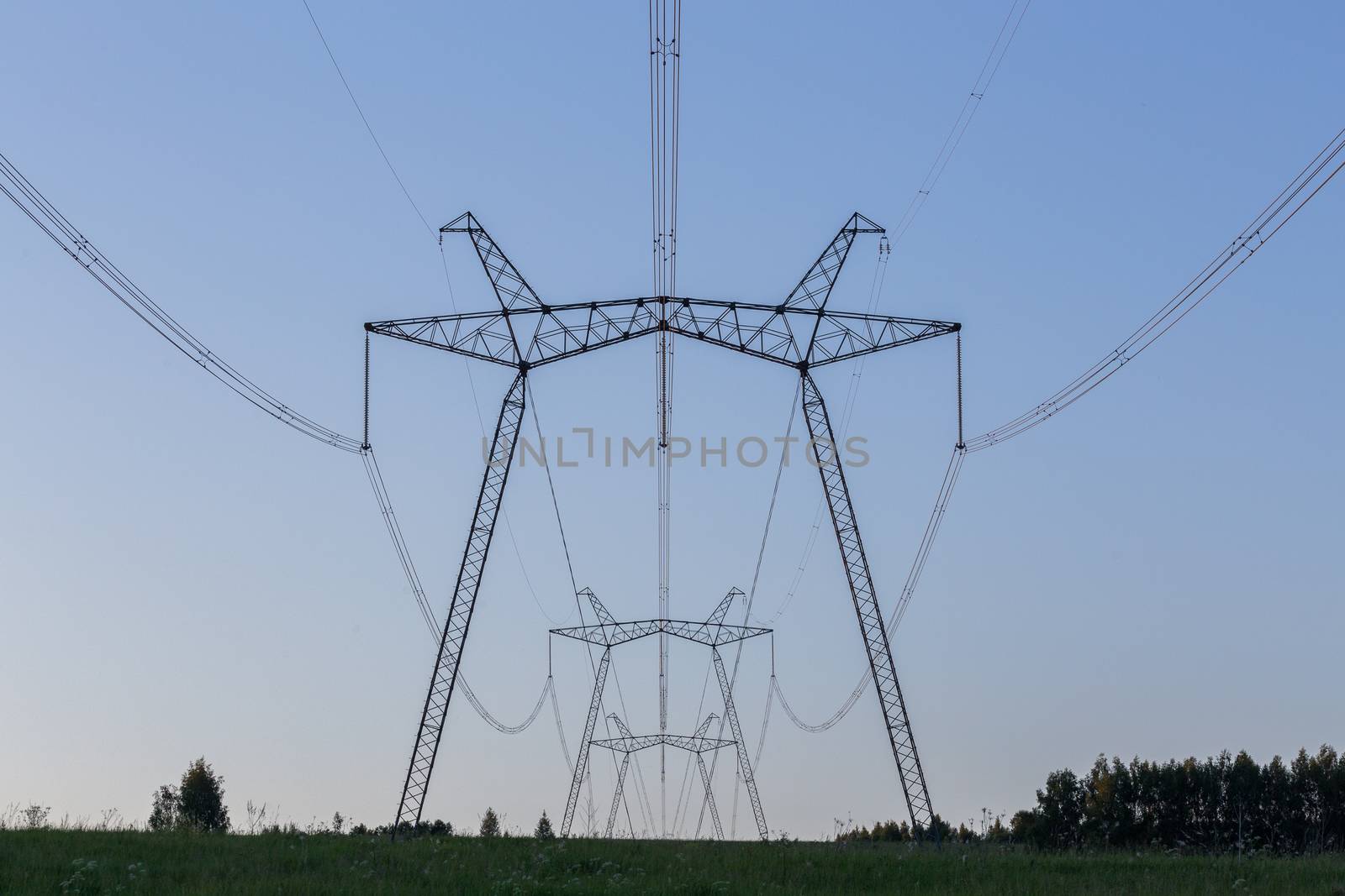 huge power line towers on field at summer evening.