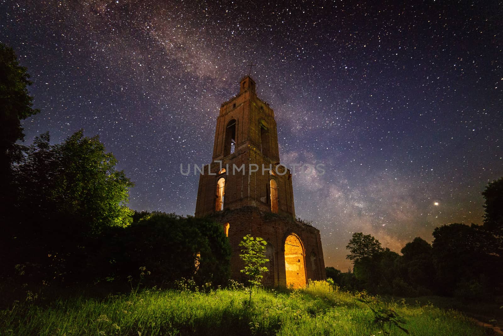 night brick bell tower ruin in forest at starry night with mystical internal light.