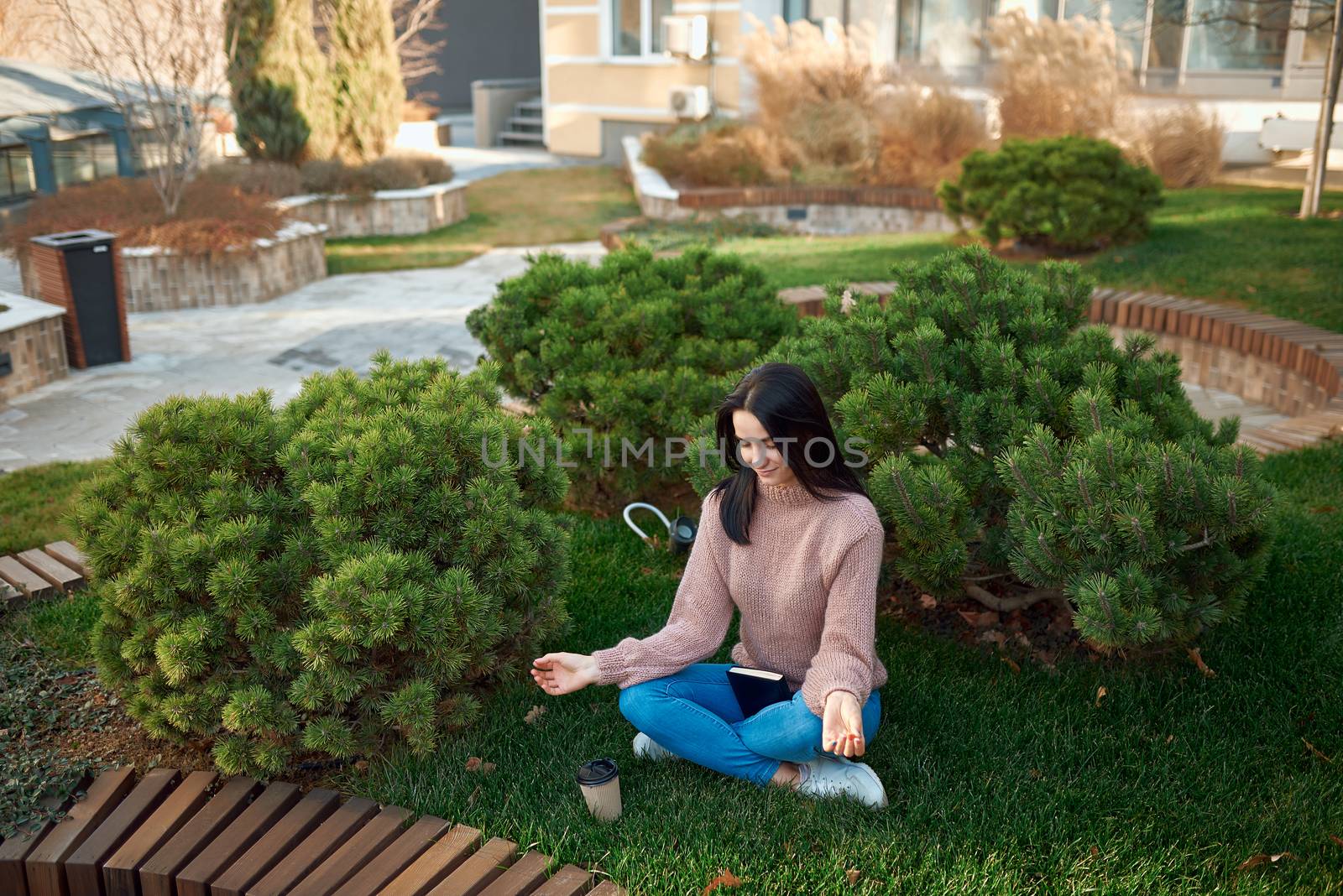 Charming lady practicing meditation on a green lawn outside of building by monakoartstudio