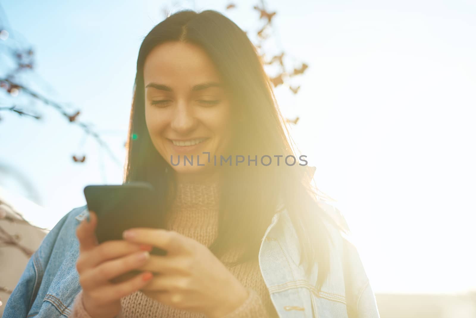 Cheerful smiling young female communicating by internet using a cellphone outdoors in a nice sunny autumn day