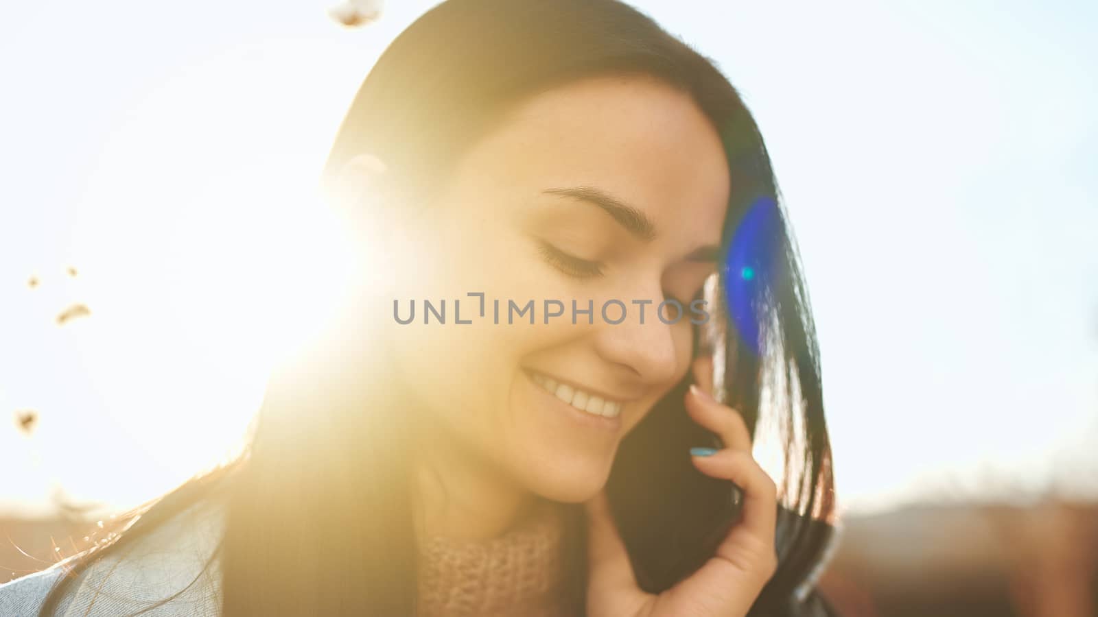Beautiful female brunette with a smartphone enjoying warm sunlight by monakoartstudio