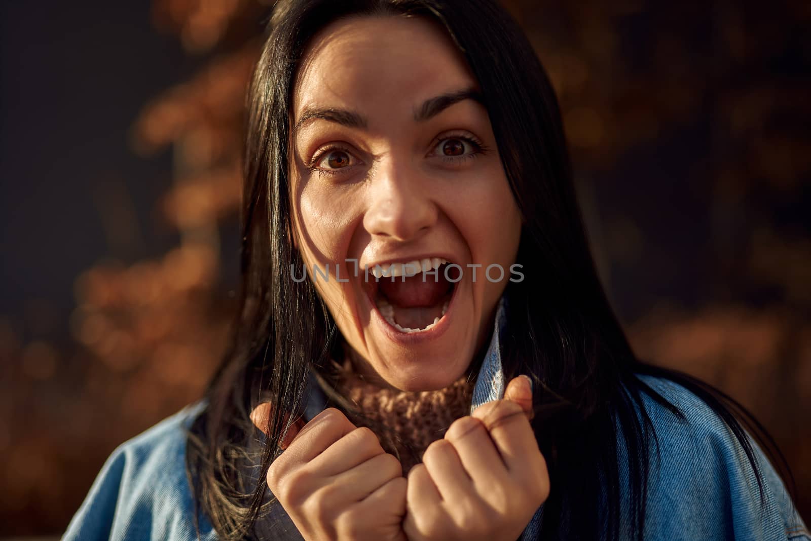 Close up portrait of a young adorable woman yelling happily while holding tightly the collar of her denim jacket