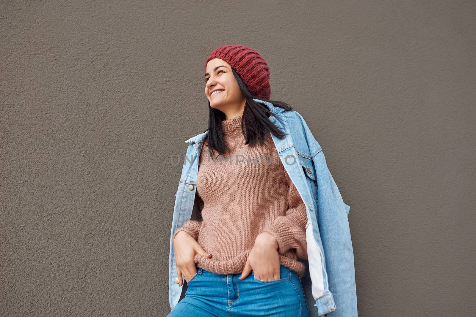 Cropped portrait of a joyful young woman in trendy casual clothing posing near the wall with her hands in pockets of jeans