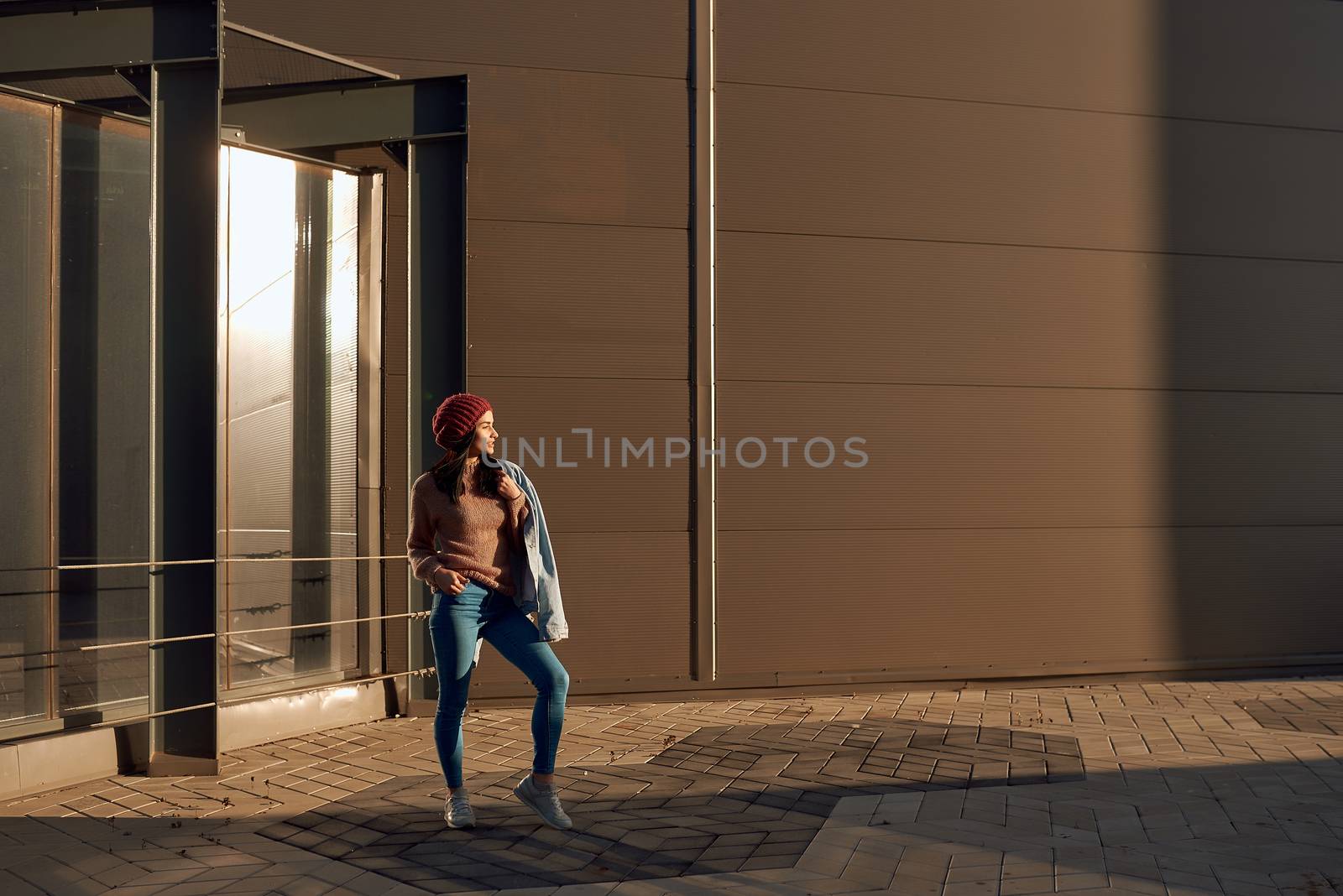 Stylish female standing in lights of a sun close to urban construction by monakoartstudio