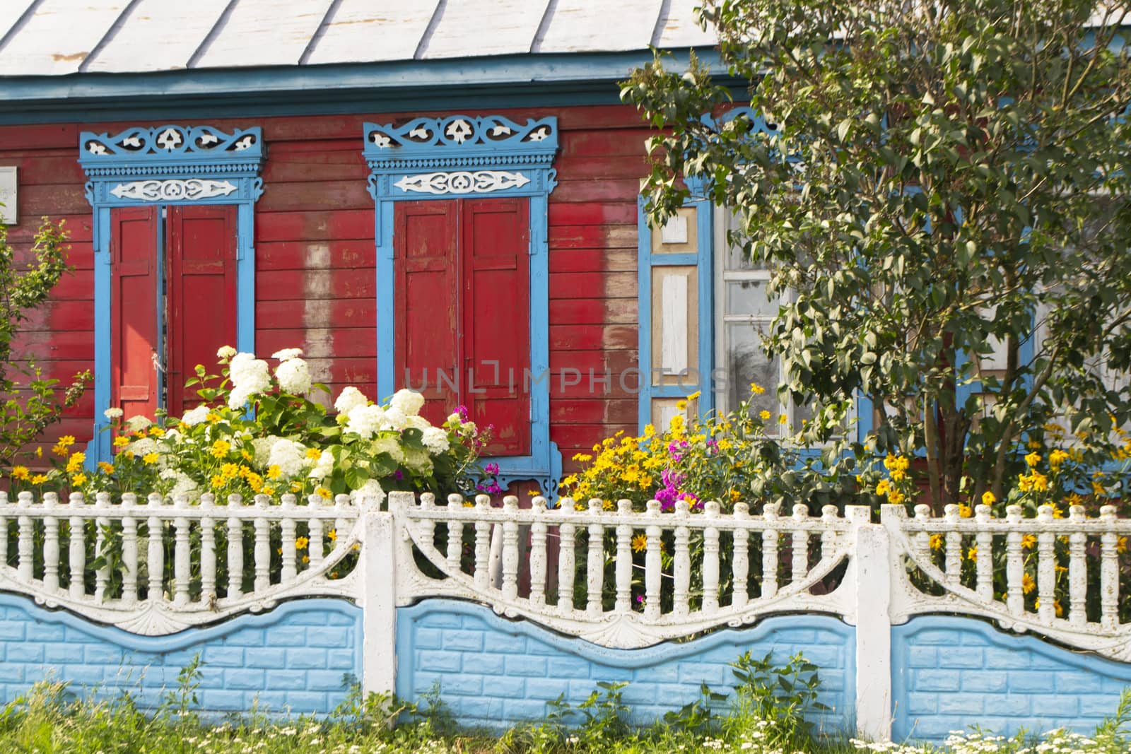 Colorful typical wooden house with ornamental carved windows in Belarus. Summer day with flowers