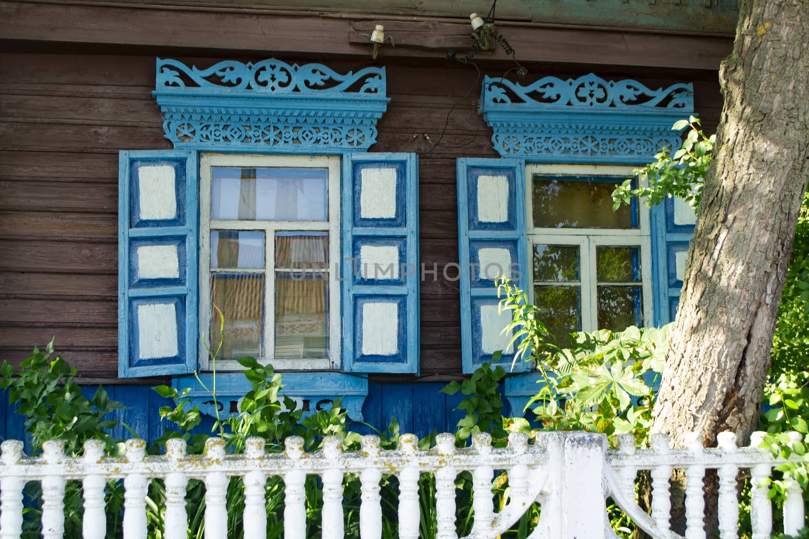 Blue figured wooden frame windows. Window frame of different shapes in the form of vertical strips and lozenges. Village in Belarus