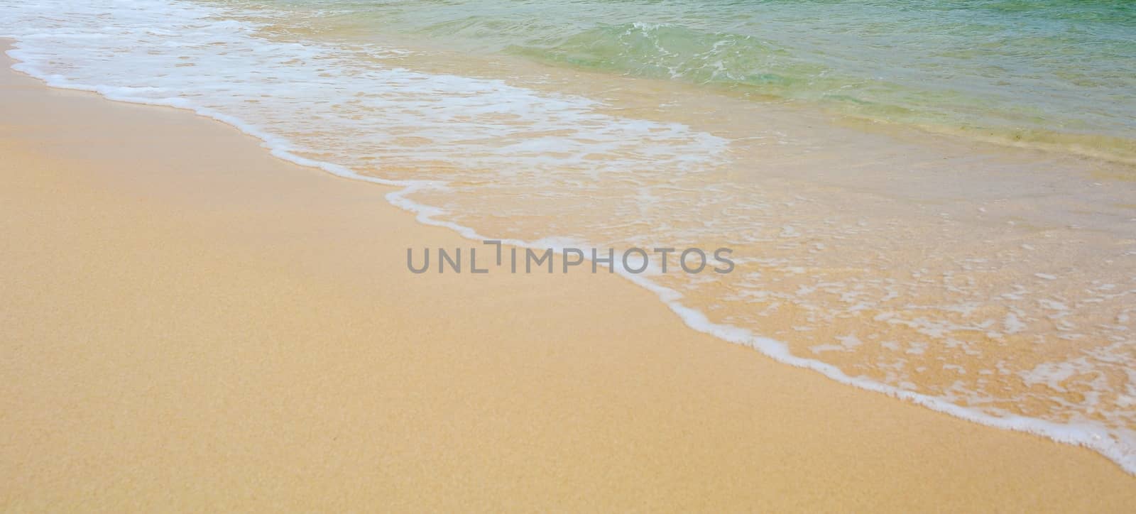 Closeup of a gold sand beach with turquoise ocean water with waves.