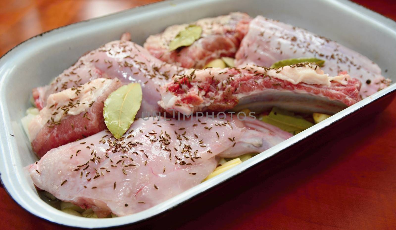 Pieces of a uncooked seasoned rabbit and pork meat in a roasting pan.