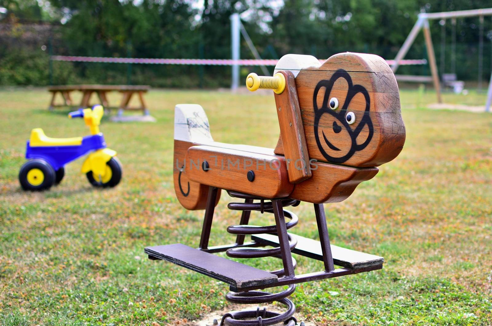 A close-up view of wooden swing on spring with plastic tricycle in the empty playground. Shallow depth of field. Focused on foreground.