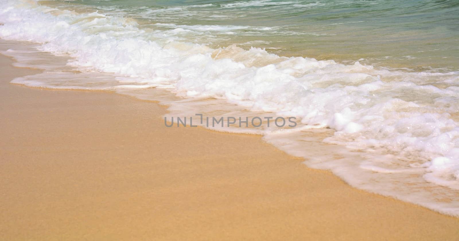 Closeup of a gold sand beach with turquoise ocean water with waves.