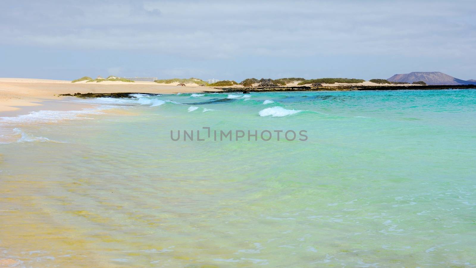 View of an empty Beach named Glass Beach with turquoise water and waves, near Corralejo town and natural dunes park on Fuerteventura island.