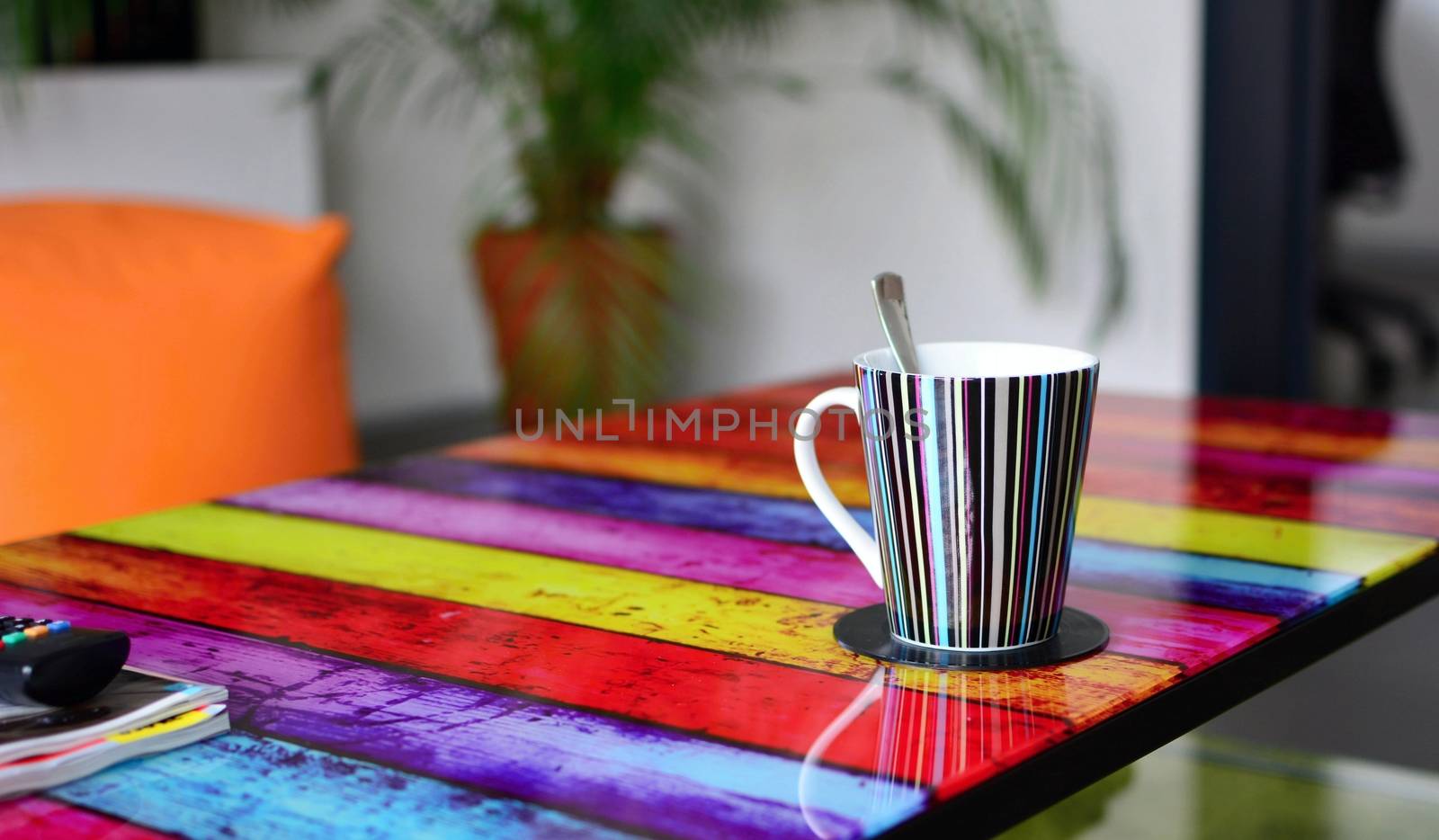 Multicolor glass table with cup of coffee in modern furnished living room. Focused on foreground with cup of coffee.