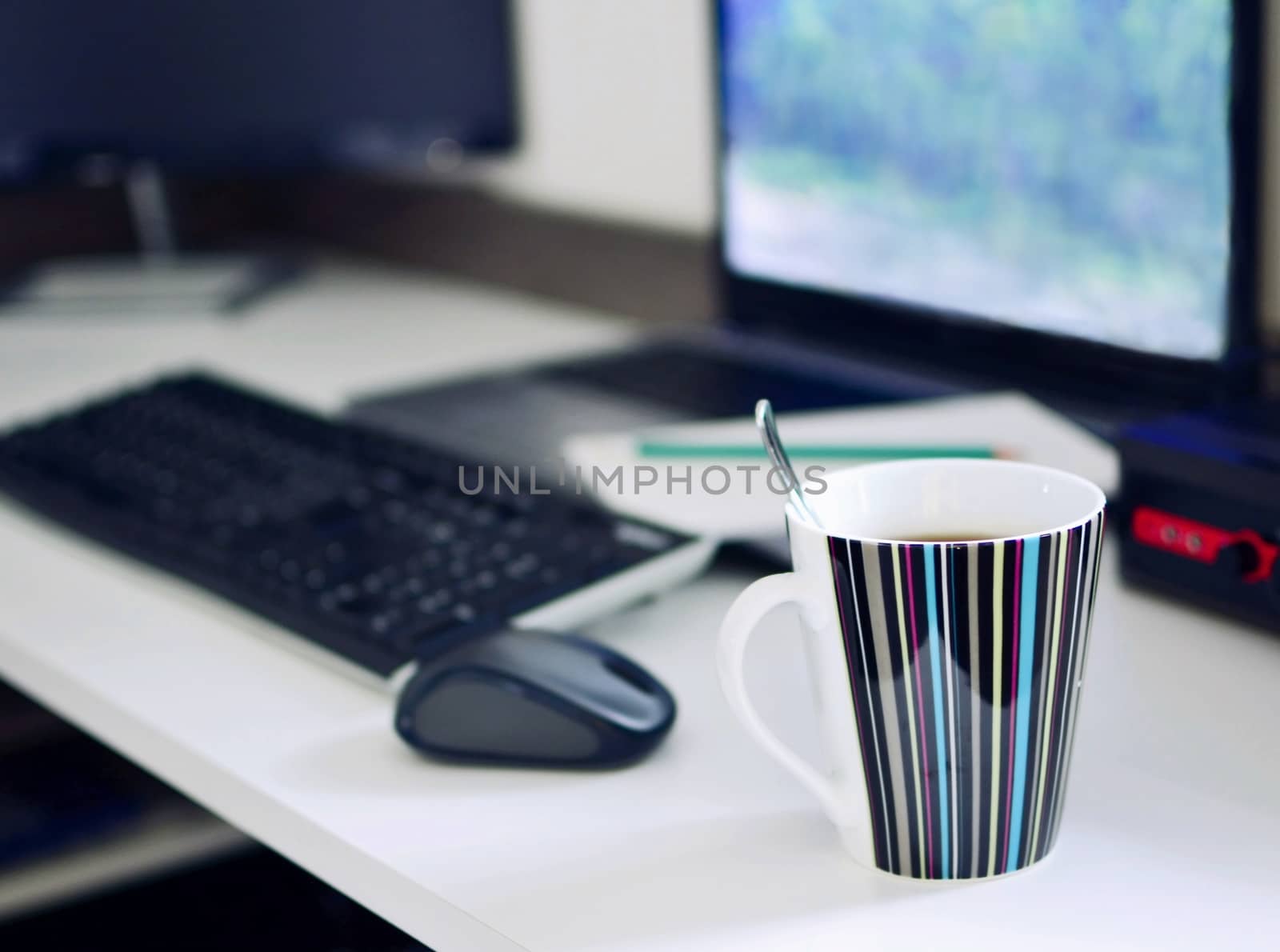 Home working desk with laptop, keyboard, mouse, notepad and cup of coffee. Working from home conceptual shot. Focused on foreground with cup of coffee.