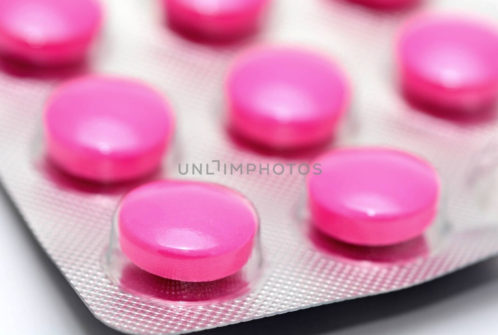 Macro shot of pink pills in blister pack over white background.