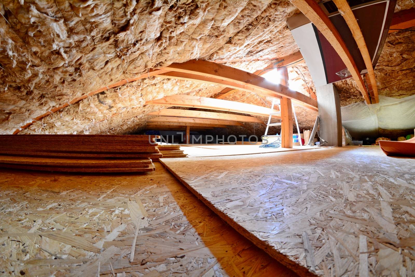 Empty house attic space with wood beams, wool roof insulation, chipboard floor and roof window with sunlight.