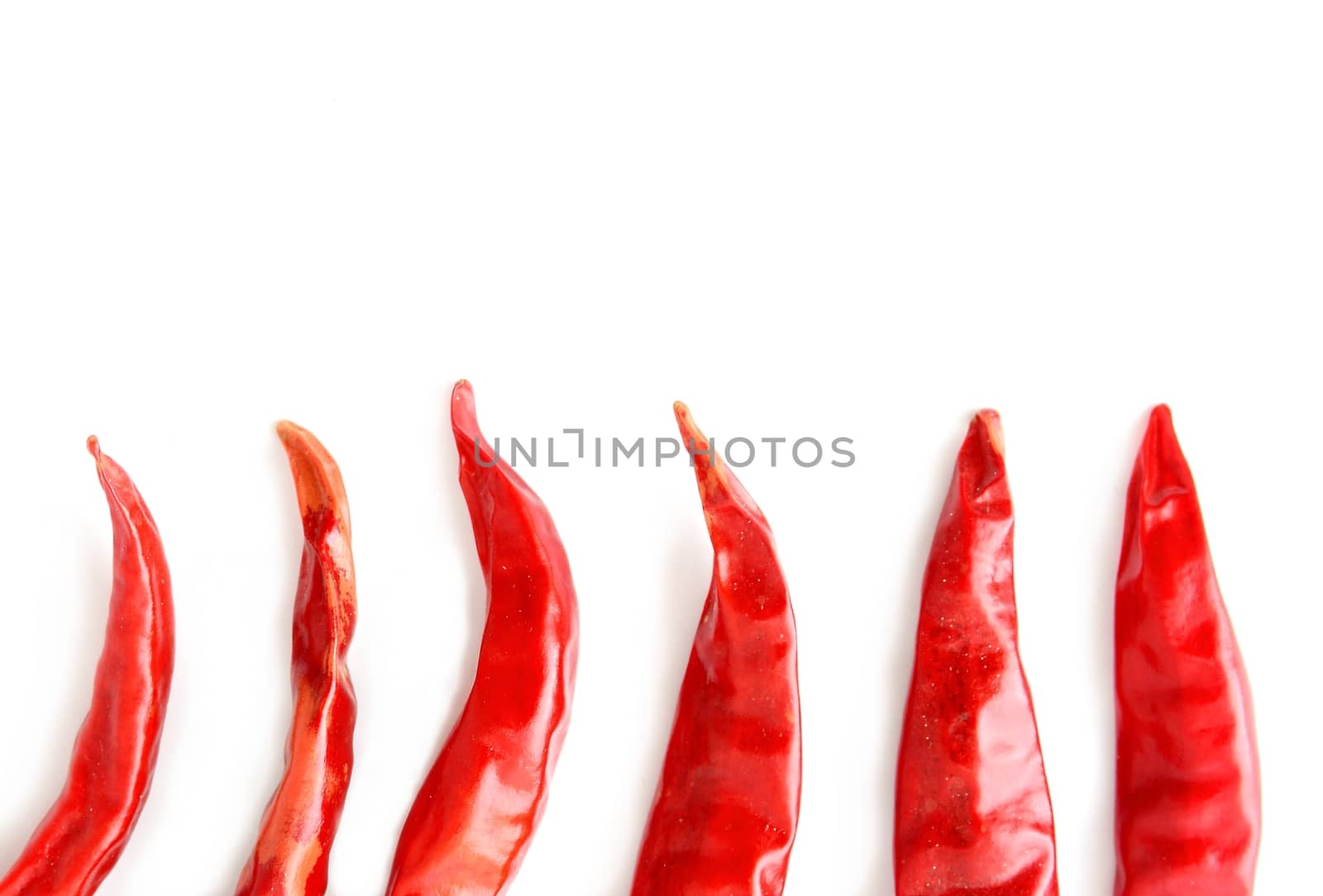 Top view of dried red hot chilli peppers halves arranged in a row. It looks like a chilli flames on white background with copy space on upper side.
