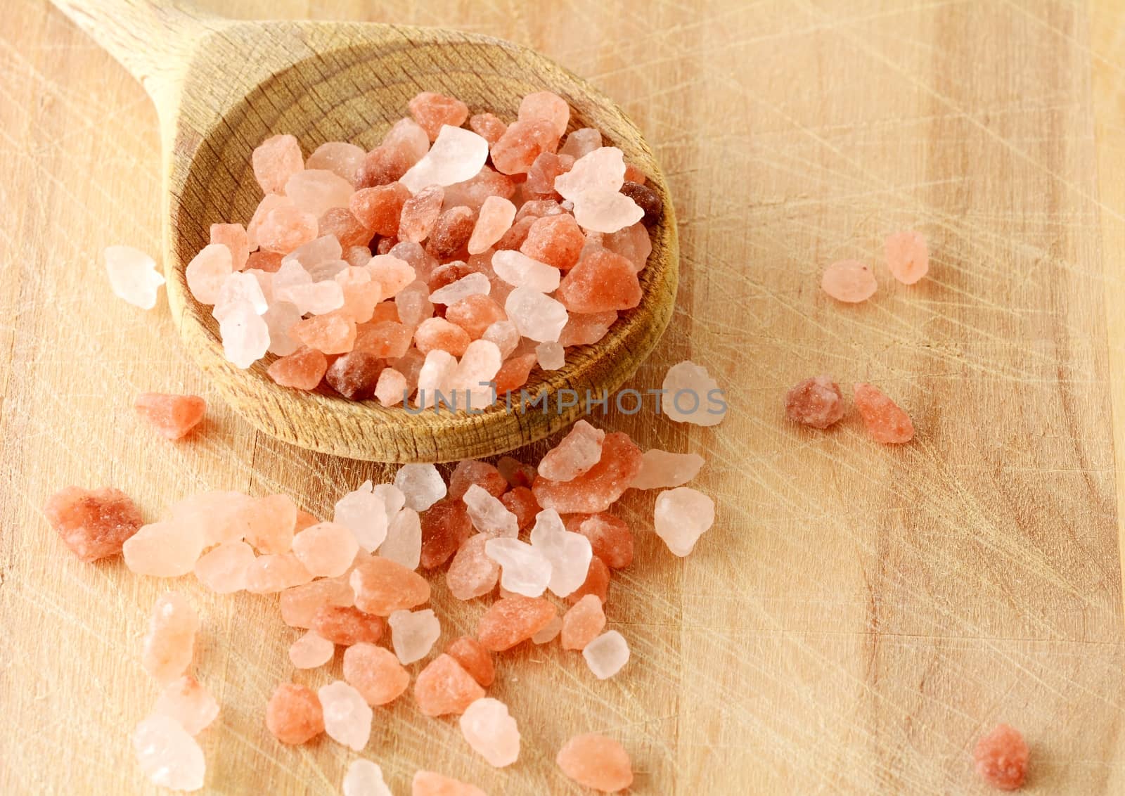 Scattered Pink Himalayan Rock Salt in Wooden Spoon on Wooden Background, top view.