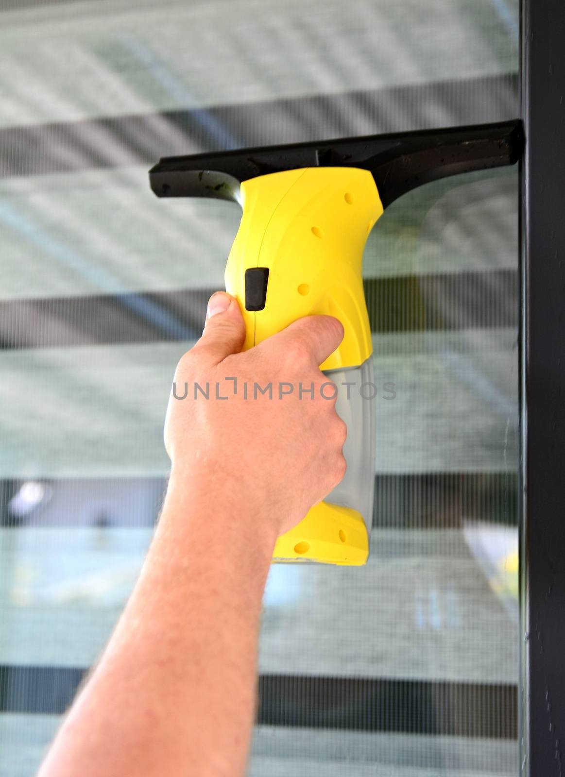 Cleaning window with cordless electrical vacuum cleaner. Man holding and using vacuum cleaner.