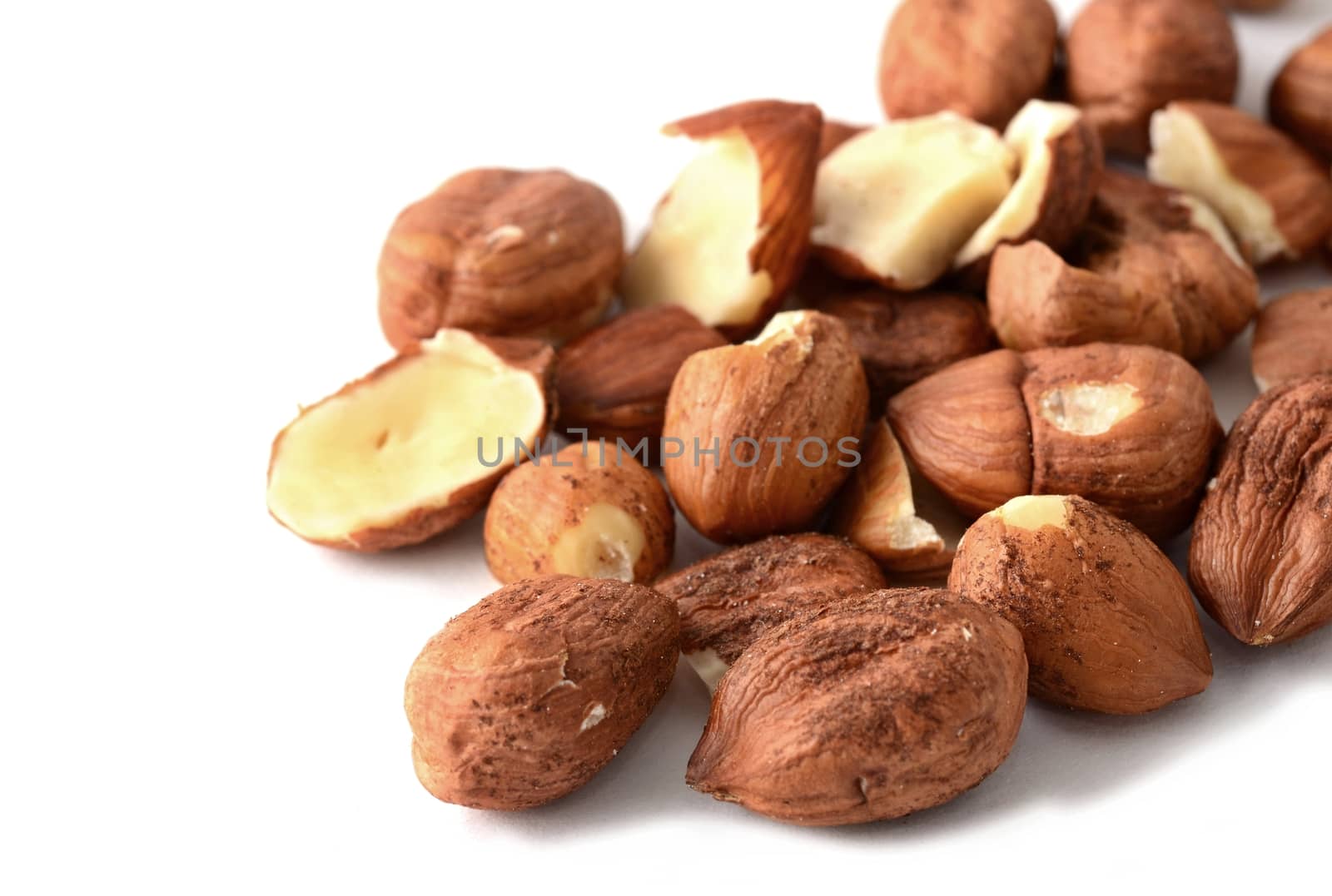 Heap of peeled scattered hazelnuts over white background.