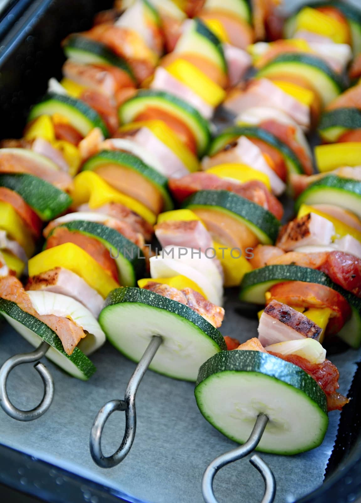 Pan full of metallic skewers with uncooked raw pork meat and vegetables ready for baking.