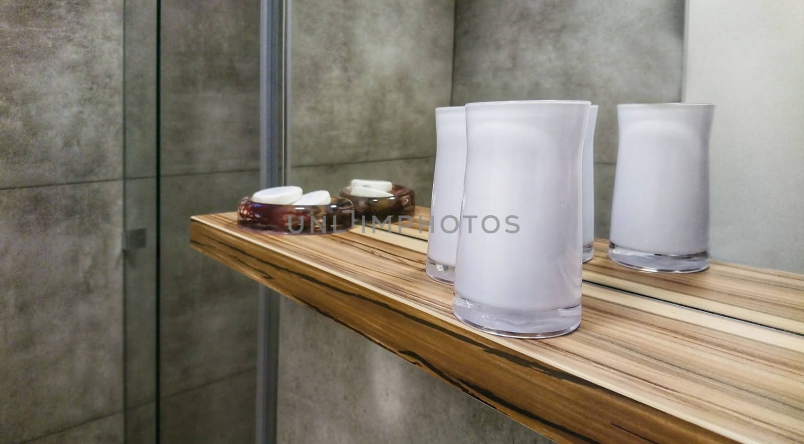 Bathroom wooden shelf with decorative candela glasses and soaps.