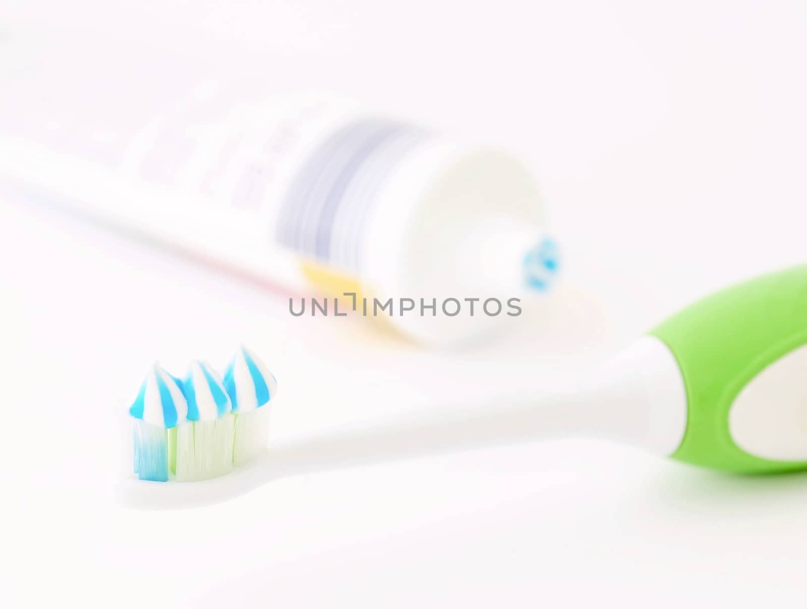 Toothbrush head with toothpaste and toothpaste tube on white background. Focused on foreground. Shallow depth of field